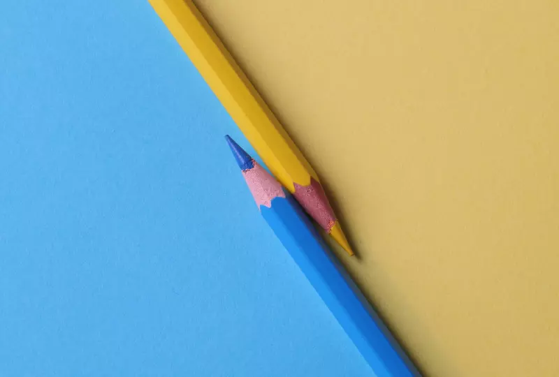 Ein gelb blaues Blatt Papier, darauf befinden sich ein blauer und ein gelber Buntstift. Symbolisch steht das Bild für das Thema Farbkontraste und Barrierefreiheit, dem Titel des dazugehörigen Blogbeitrages.